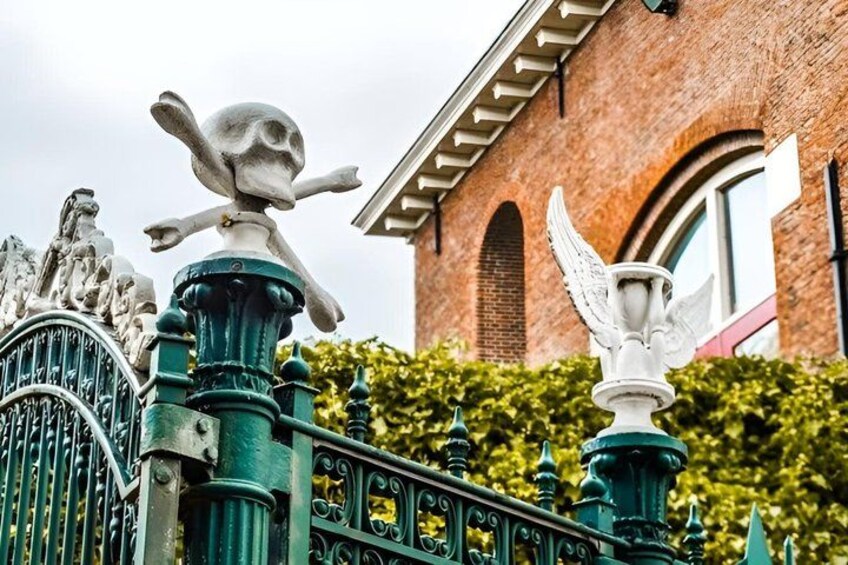 A wrought iron fence with decorative elements, a brick building, and a statue of an angel. 1