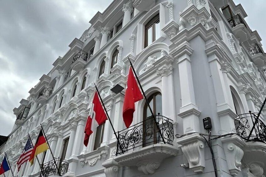 A white building with ornate architecture, multiple flags, and a balcony. 2