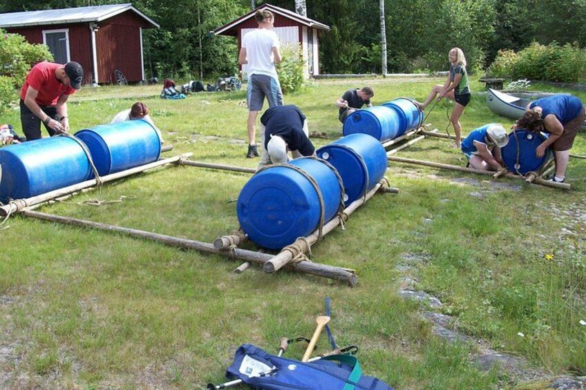 People assembling large blue barrels on a grassy field with a shed in the background. 5