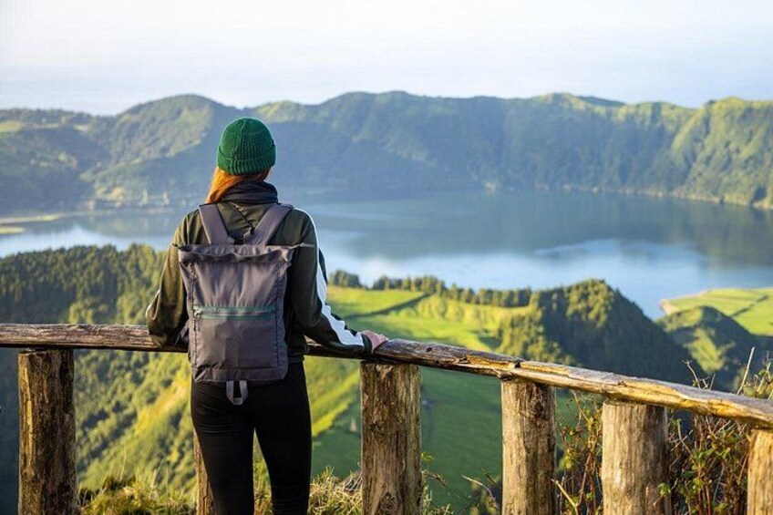 A person standing on a wooden railing overlooking a lake surrounded by hills. 4