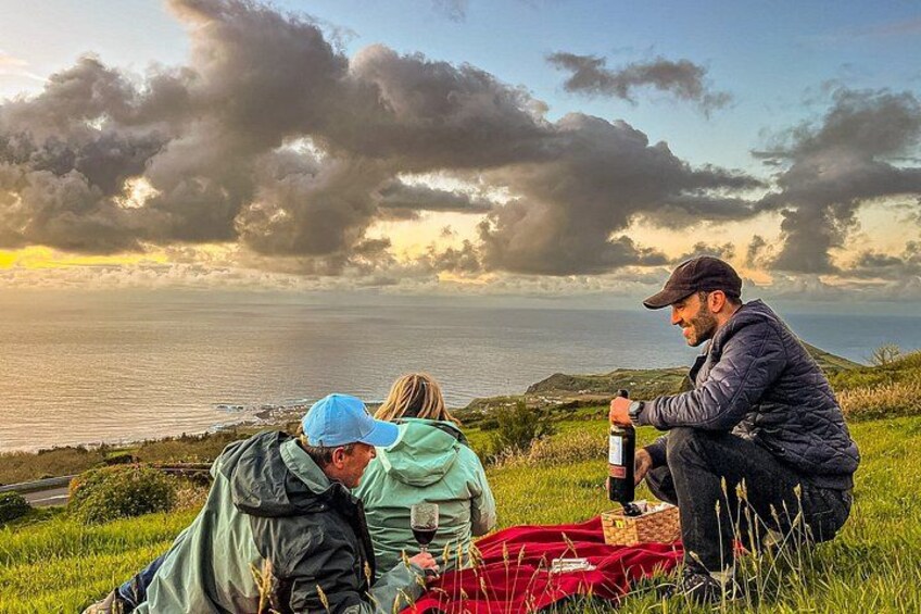Three people sitting on a grassy hill overlooking a body of water during sunset. 3