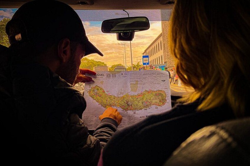 A person holding a map, another person looking at the map, and a street sign in the background. 2