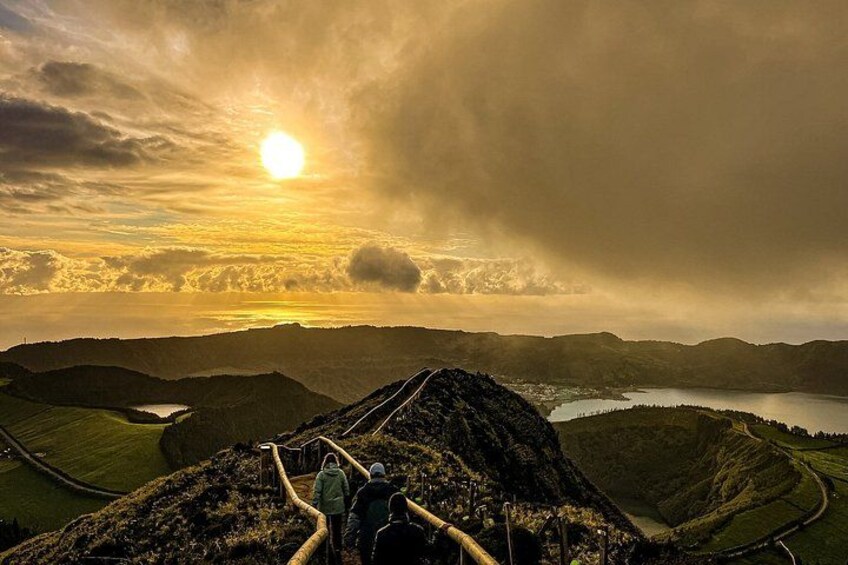 A mountainous landscape with a winding path, a lake, and a sunset. 1