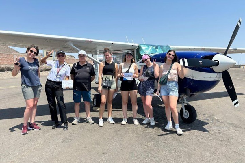 A group of people posing in front of a small blue and white airplane on a tarmac. 1