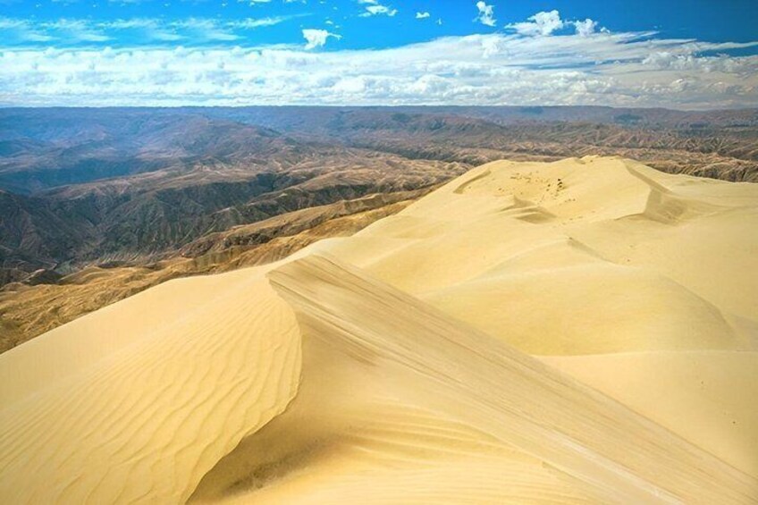 A vast desert landscape with prominent sand dunes and a distant mountain range under a clear sky. 3