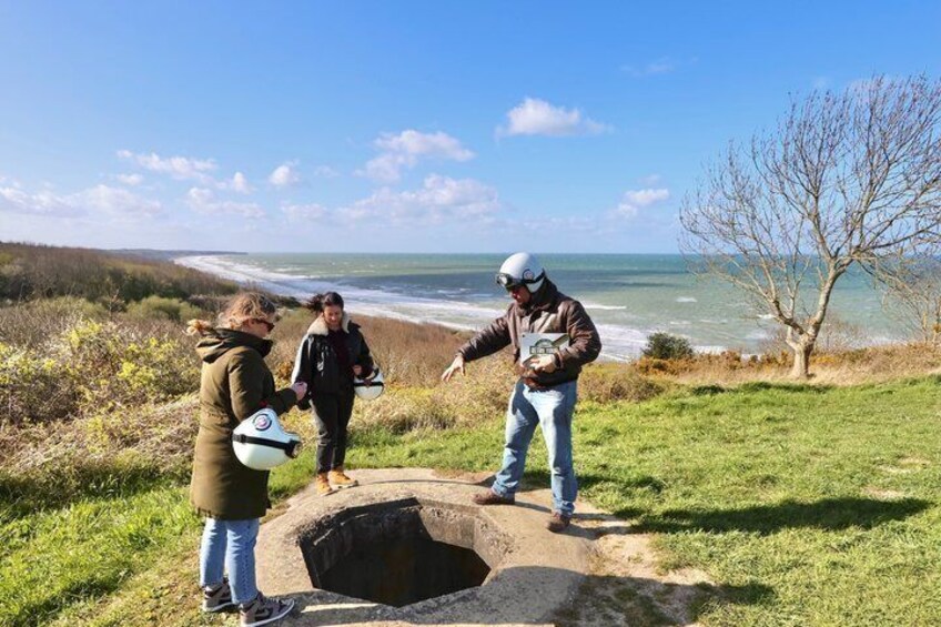 Three people standing by a large hole in the ground with a coastal view in the background. 3