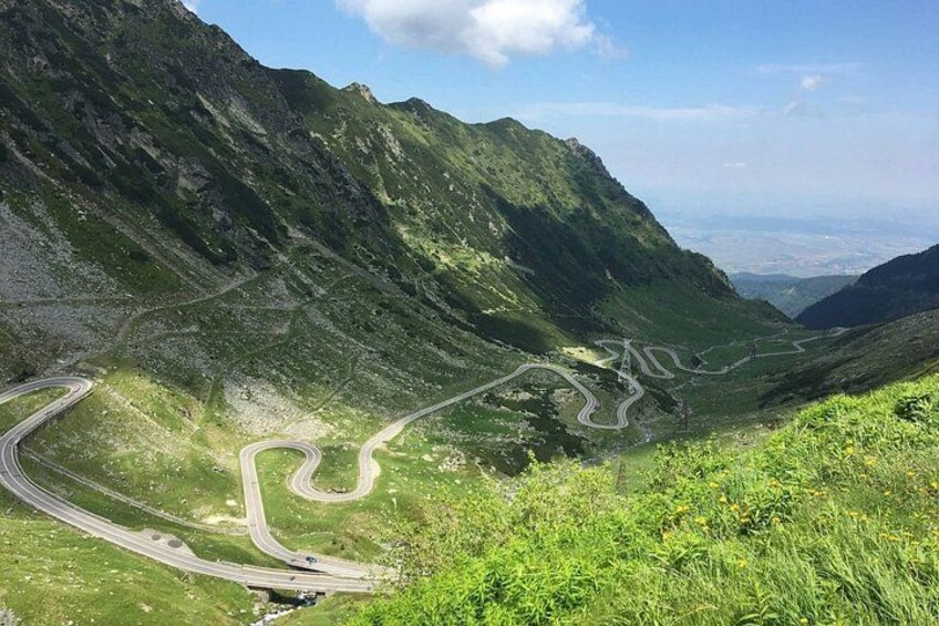 A winding mountain road with green vegetation and rocky terrain. 3