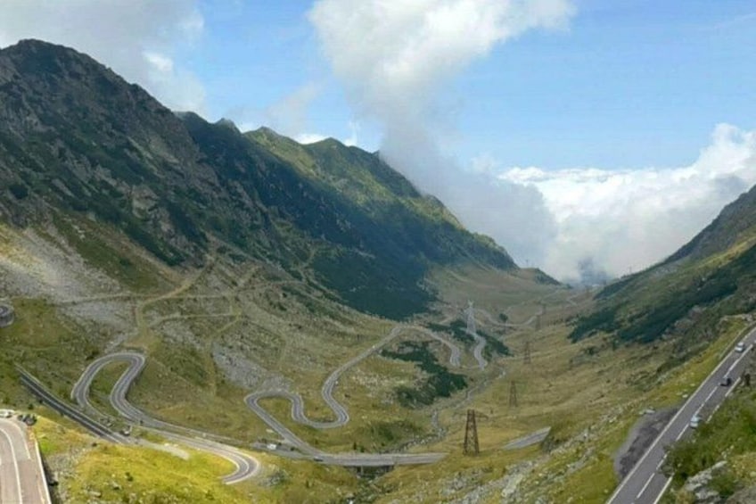 A winding mountain road with multiple lanes, surrounded by green hills and a clear sky. 1