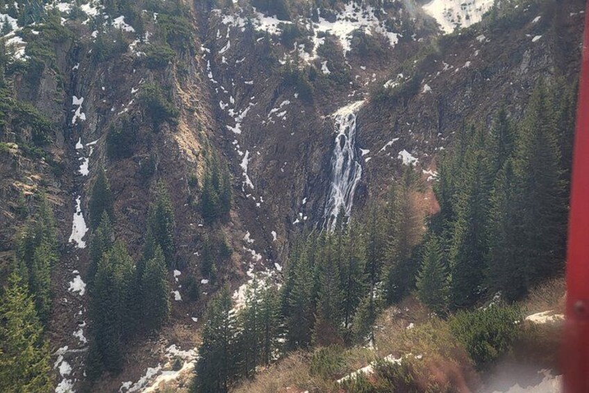 A waterfall cascading down a rocky mountain slope surrounded by dense coniferous forest. 5