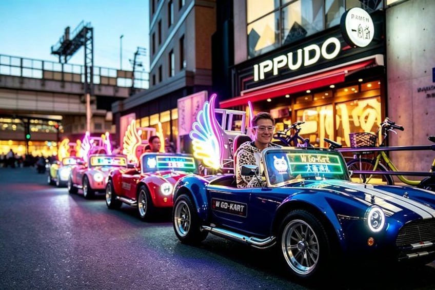 A row of classic cars parked on a street with neon signs and a building with signage in the background. 1