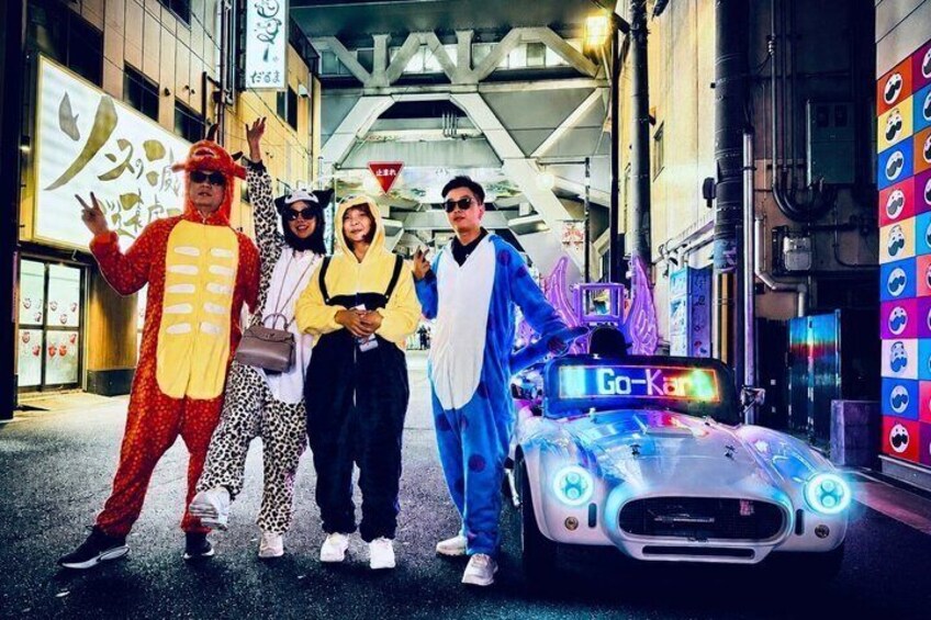 A group of people in costumes, a sports car, and a Go-Kart sign in an urban setting. 2