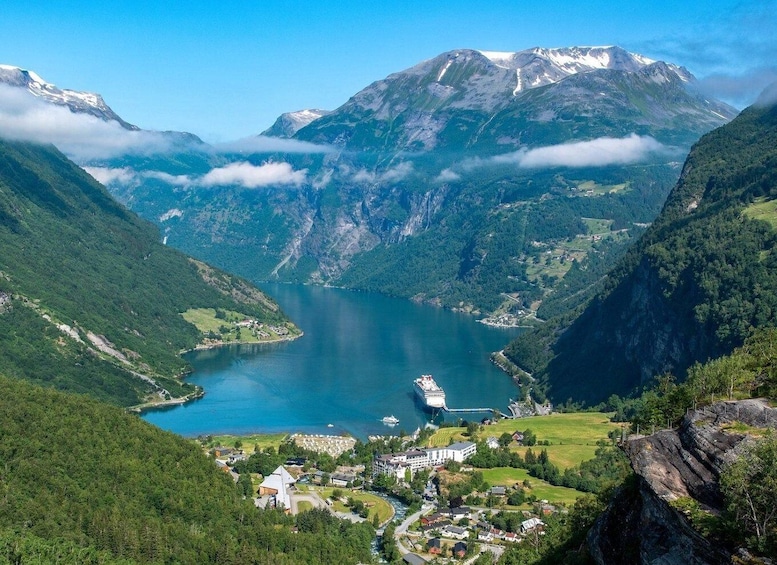 A lake surrounded by mountains, a cruise ship docked at a pier, and a small village with houses and greenery. 2