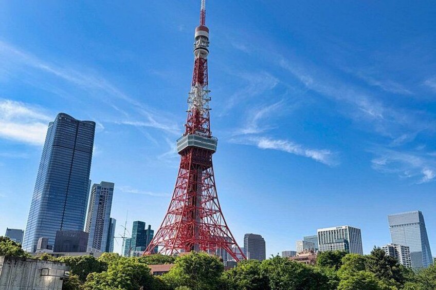 A red tower with a white spire, surrounded by modern skyscrapers and greenery. 2