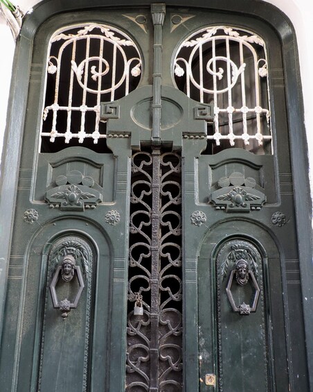 A detailed wrought iron gate with decorative elements and two door knockers. 3