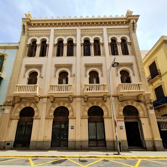 A beige building with ornate arches and balconies, featuring multiple windows and a street lamp. 5