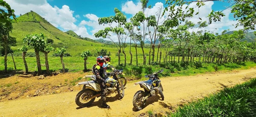 Two dirt bikes on a dirt road with green hills in the background. 4
