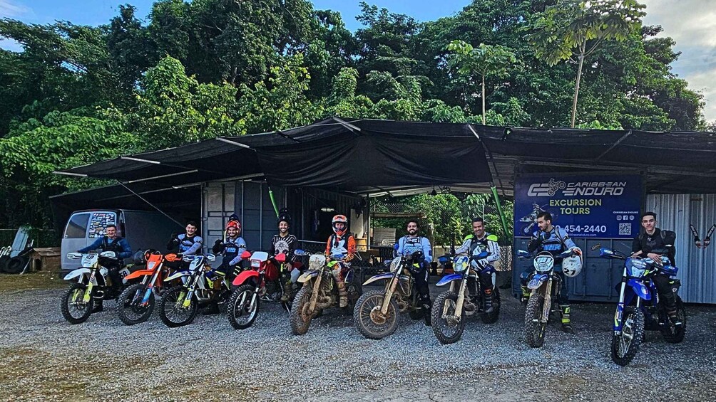 A group of motocross riders posing with their bikes in front of a garage. 1