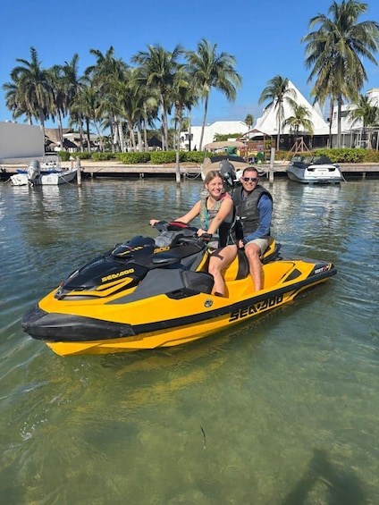 Two people on a yellow Sea-Doo jet ski in clear water with palm trees and buildings in the background. 5