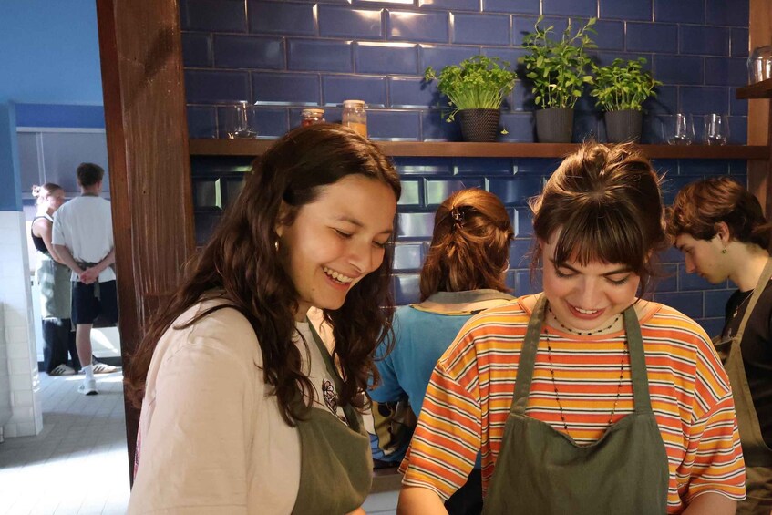 A group of people in a kitchen area with blue tiled walls and potted plants on shelves. 3