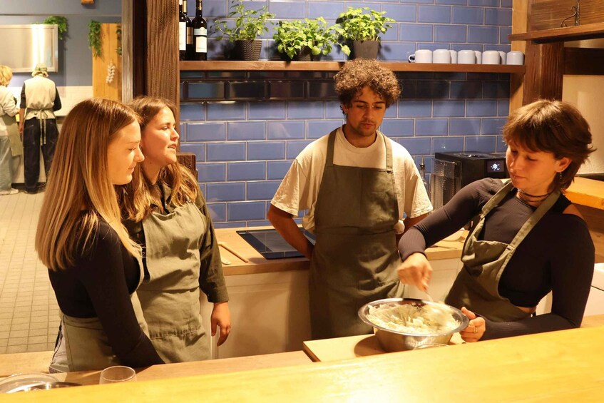 A kitchen with blue tiles, a person in an apron preparing food, and another person observing. 4