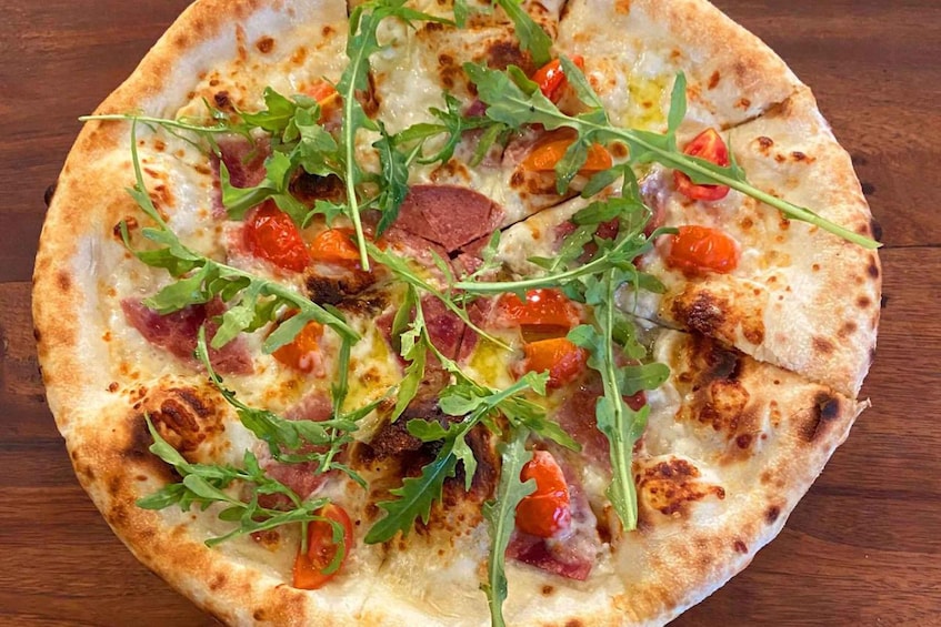 A pizza with arugula, tomatoes, and ham on a wooden table. 3