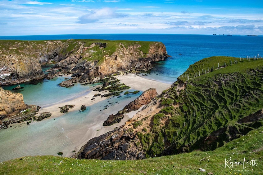 A coastal landscape with rocky cliffs, a sandy beach, and a clear blue sea. 1