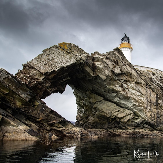 A lighthouse through a natural rock arch over water. 2
