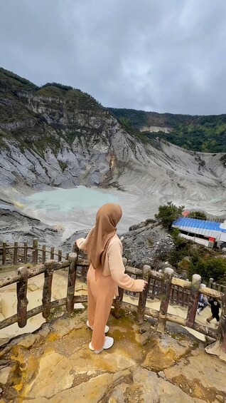 A person standing on a rocky ledge overlooking a geothermal area with a small pool of water. 1