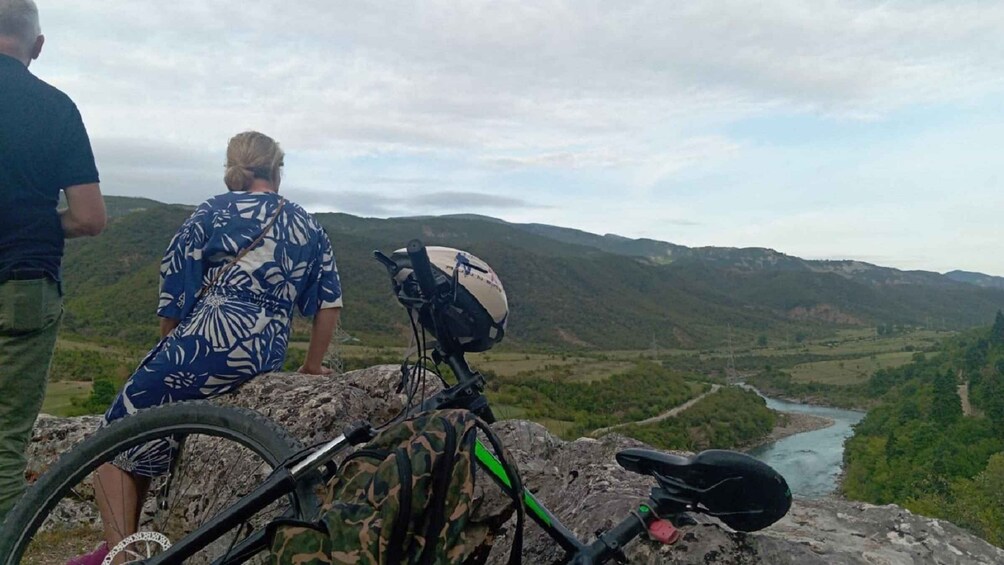 Two people overlooking a valley with a river, mountains, and a bicycle. 5