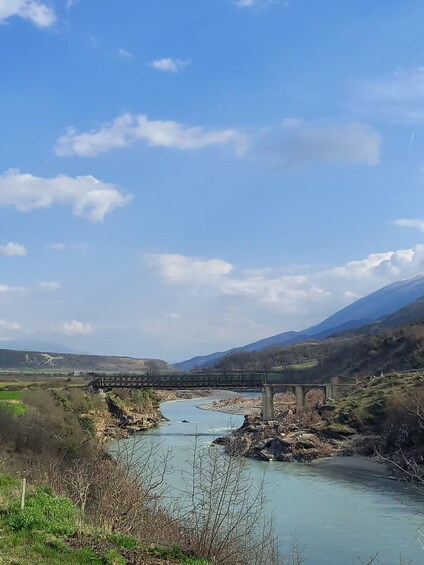 A river flowing under a bridge, surrounded by hills and a clear sky. 4