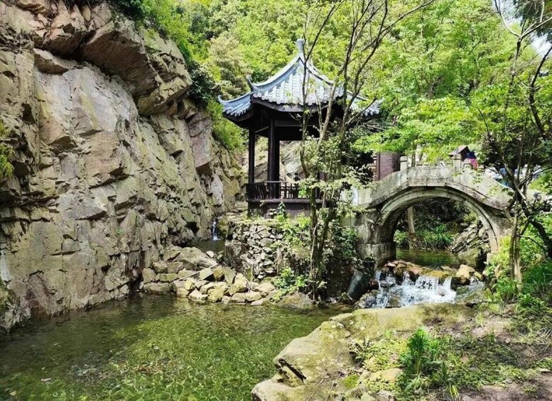 A traditional pavilion, a stone bridge, and a clear water stream in a forested area. 1