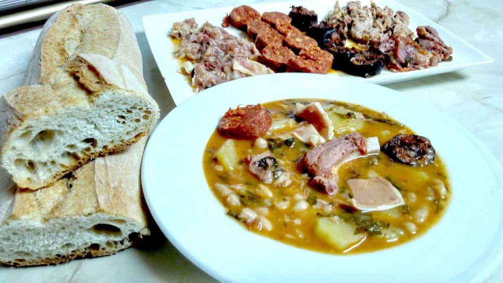 A meal with bread, a soup with beans and meat, and a plate of sausages. 2