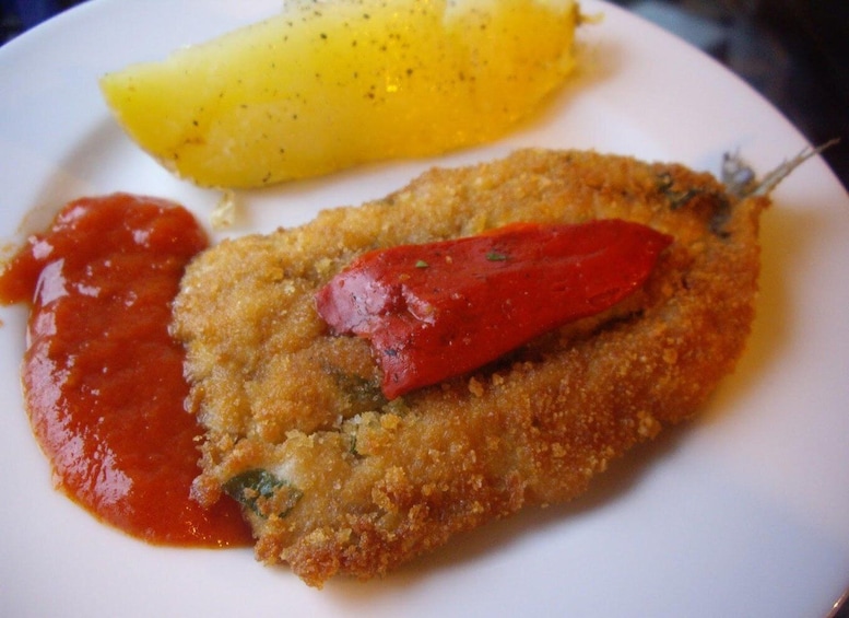 A breaded and fried cutlet with a red pepper, ketchup, and a boiled potato on a white plate. 3