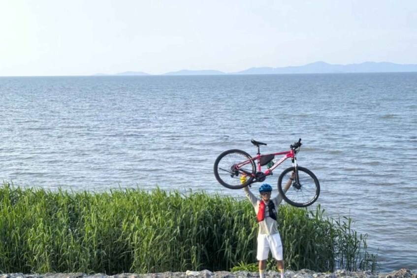 A person holding a bicycle by the water's edge. 1