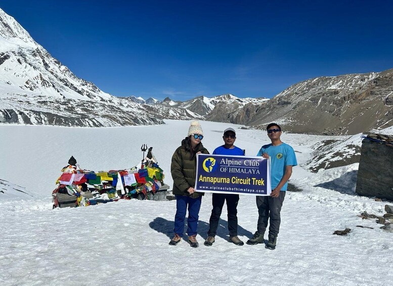 En grupp människor står på ett snöigt berg, och i bakgrunden syns en skylt för Alpinföreningens vandringsled runt Annapurna i Himalaya. 1