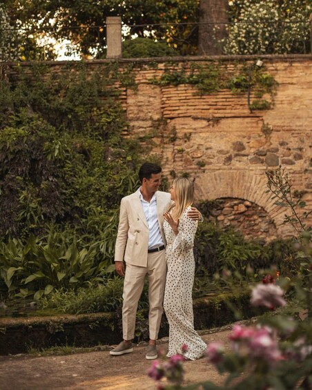 A couple standing in a garden with a stone wall and greenery in the background. 1