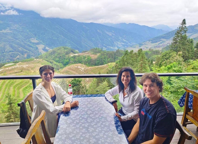 Drei Personen sitzen an einem Tisch mit Blick auf eine malerische Berglandschaft im Hintergrund. 4