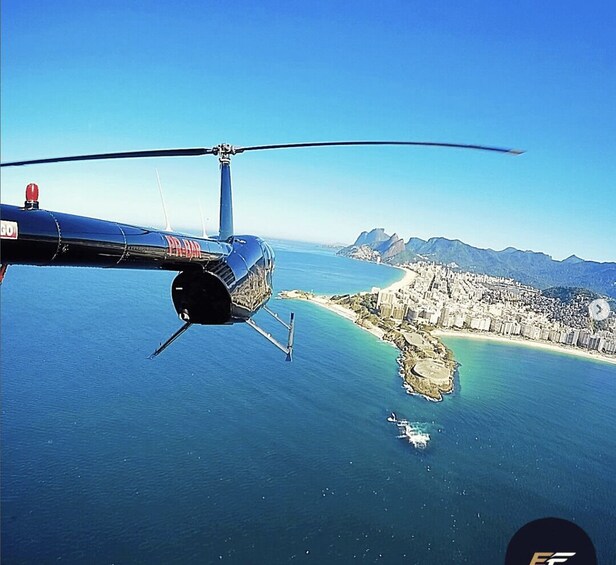 A helicopter flying over a coastal city with a clear view of the ocean and mountains in the background. 2