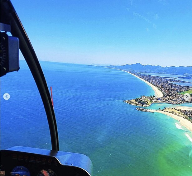 A helicopter's cockpit view over a coastal city with a clear blue sky. 4