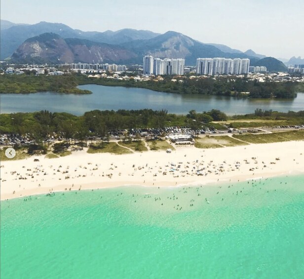 A coastal cityscape with a beach, clear turquoise waters, and a backdrop of mountains. 1