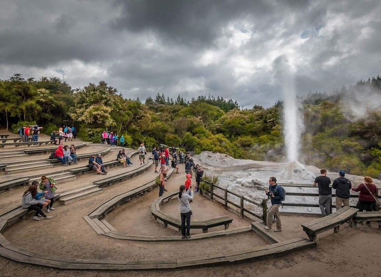 A geothermal area with a geyser, surrounded by benches and visitors. 1