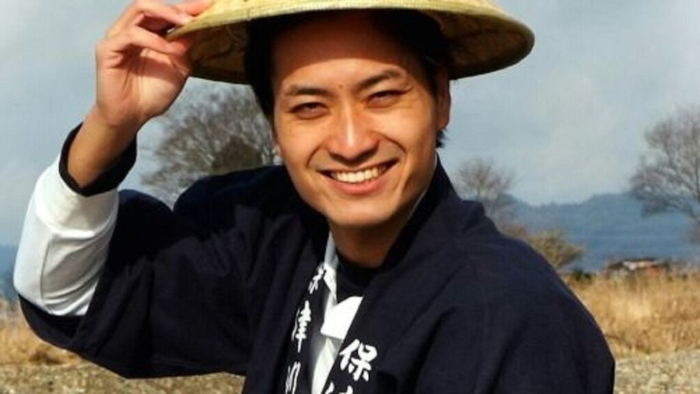 A person wearing a straw hat and a dark jacket with white text. 3