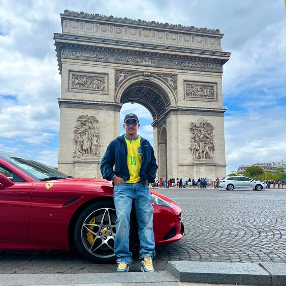 A man standing in front of the Arc de Triomphe with a red Ferrari parked beside him. 5