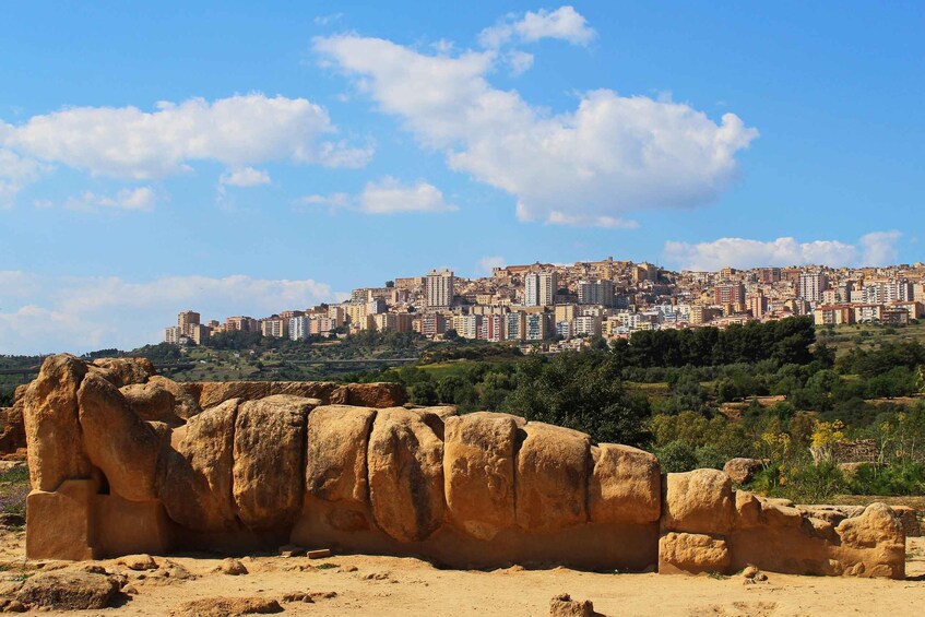 A desert landscape with a large rock formation in the foreground and a cityscape in the background. 2