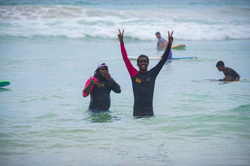 Two people in the water with surfboards, one raising their arms in victory. 2