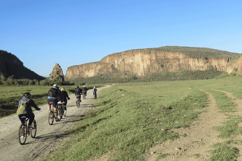 A group of cyclists on a dirt path with a large cliff in the background. 1