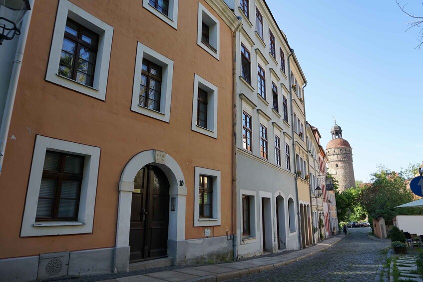 A cobblestone street lined with historic buildings, one with a tower in the background. 2