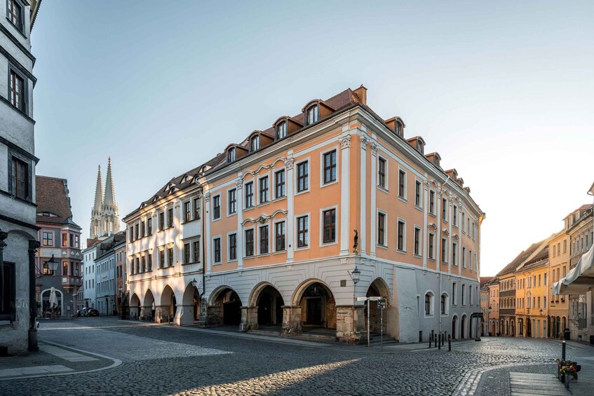 A cobblestone street with historic buildings, a church spire, and a statue. 3