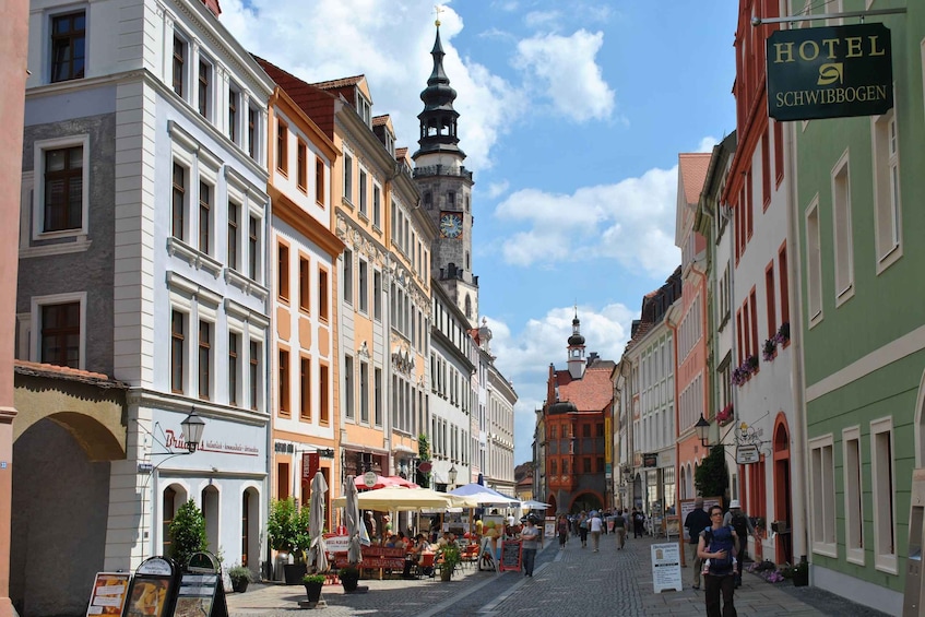 A cobblestone street lined with historic buildings, a prominent clock tower, and a sign for Hotel Schwibbogen. 1