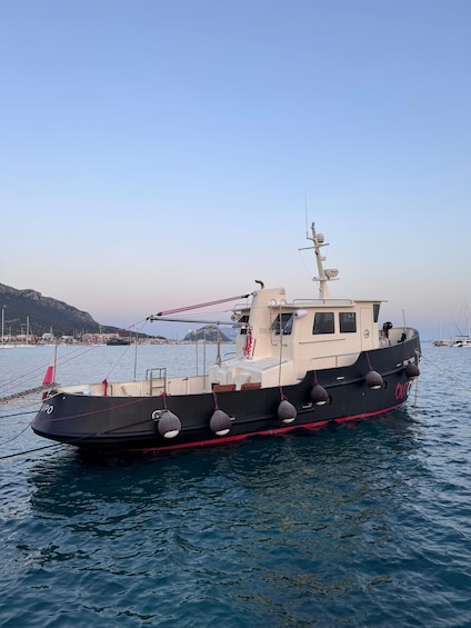 A black and white boat named 'Outo' docked at a marina with a clear sky and a mountainous landscape in the background. 1